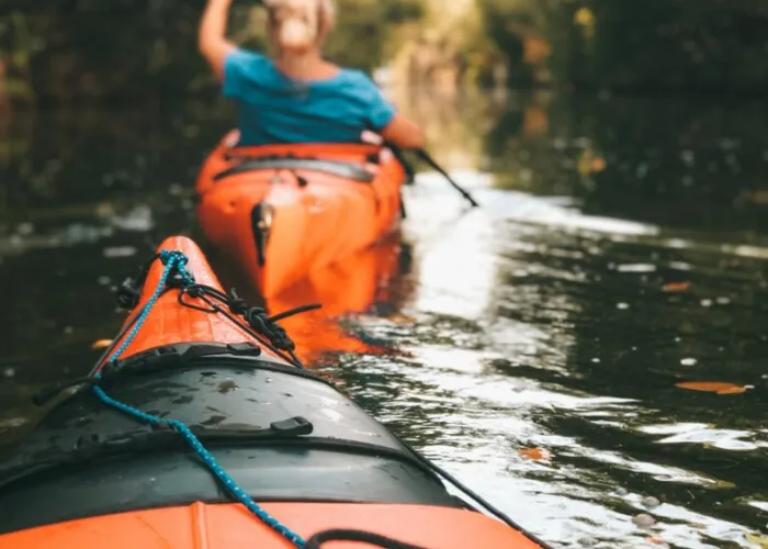 View from a kayak on the water with a person in a kayak in front paddling